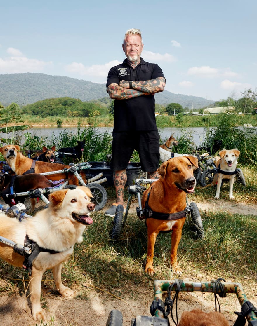 Michael J. Baines standing with rescued dogs in wheelchairs at The Man That Rescues Dogs sanctuary in Chonburi, Thailand.